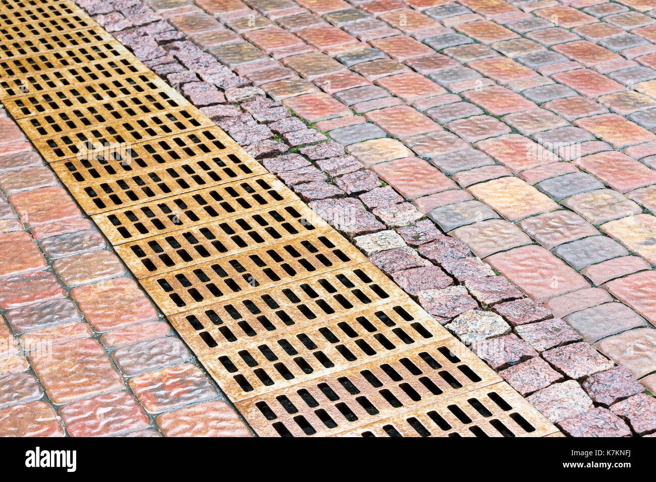 Rostiges Metall Abwasserkanal Rost für Abflusssystem auf dem nassen Kopfsteinpflaster Bürgersteig Stockfoto