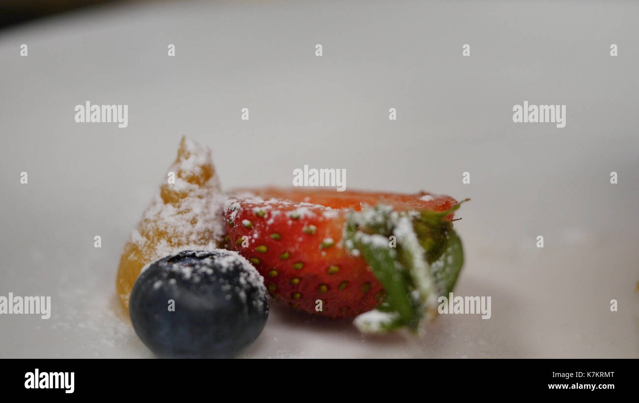 Erdbeeren und Blaubeeren mit Puderzucker Streuseln. Das Streuen von Puder auf die Erdbeeren, Blaubeeren Stockfoto