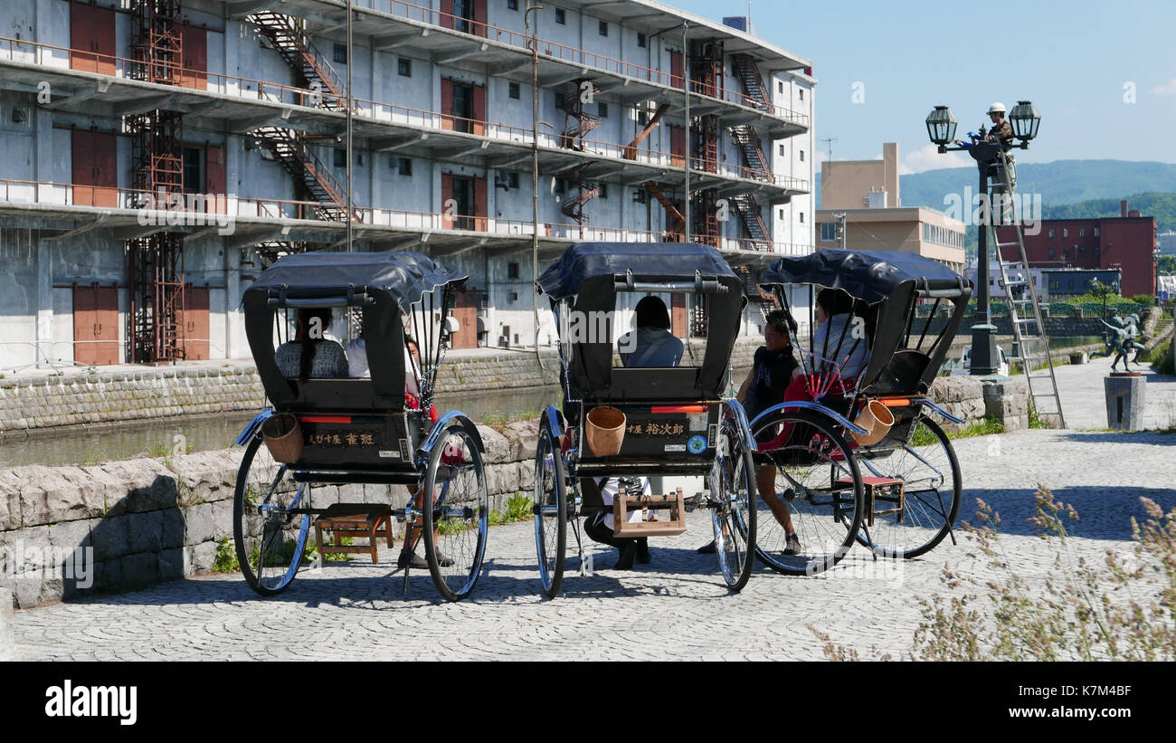 Rikscha Tour Guides Futter bis Alt, Schwarz Rikschas in der Nähe von Otaru Kanal für Gruppe Foto von mittleren Alters japanischen Touristinnen. Bunte rote Decken. Stockfoto