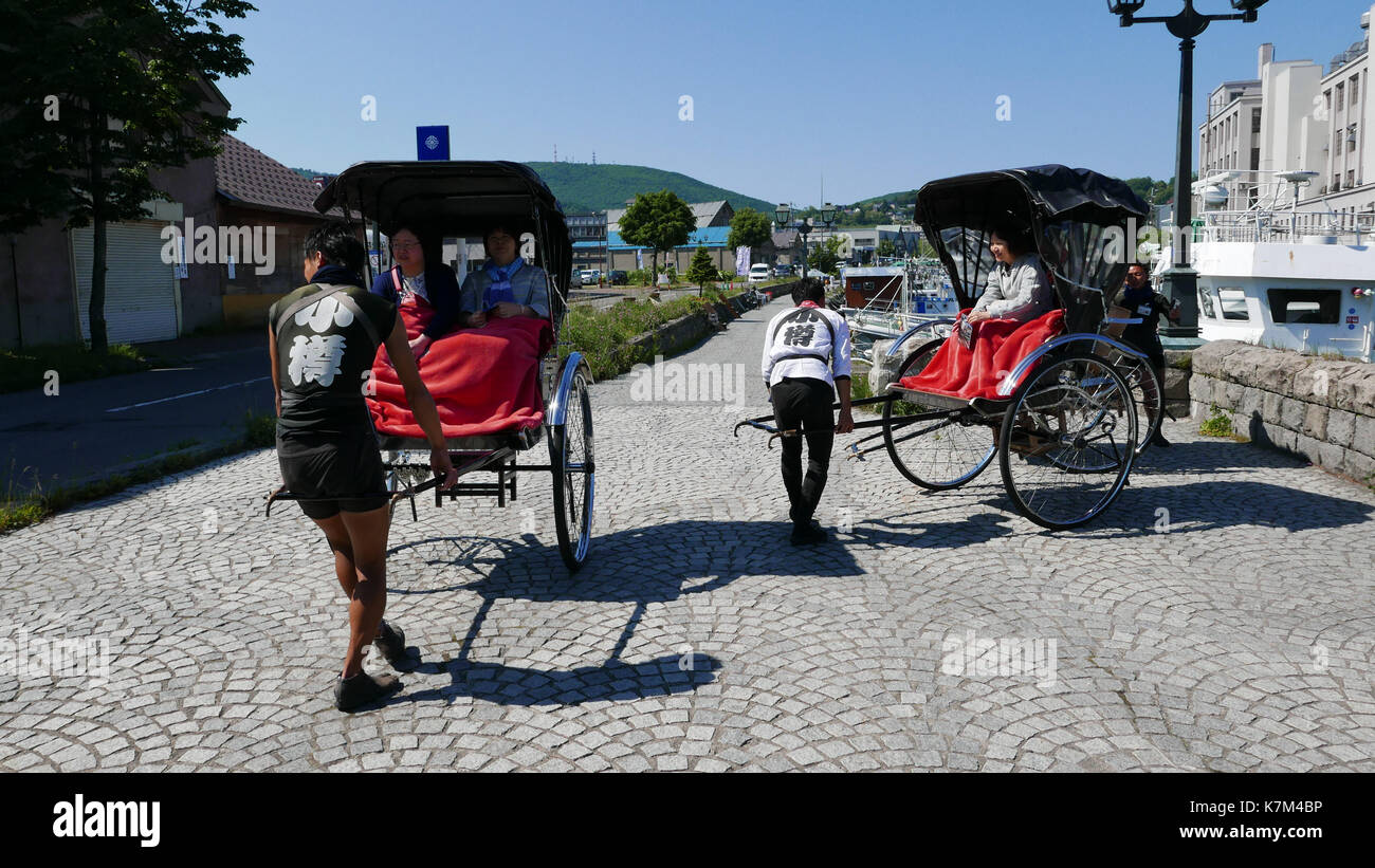 Rikscha Tour Guides Futter bis Alt, Schwarz Rikschas in der Nähe von Otaru Kanal für Gruppe Foto von mittleren Alters japanischen Touristinnen. Bunte rote Decken. Stockfoto