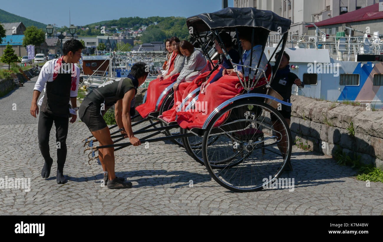 Rikscha Tour Guides Futter bis Alt, Schwarz Rikschas in der Nähe von Otaru Kanal für Gruppe Foto von mittleren Alters japanischen Touristinnen. Bunte rote Decken. Stockfoto