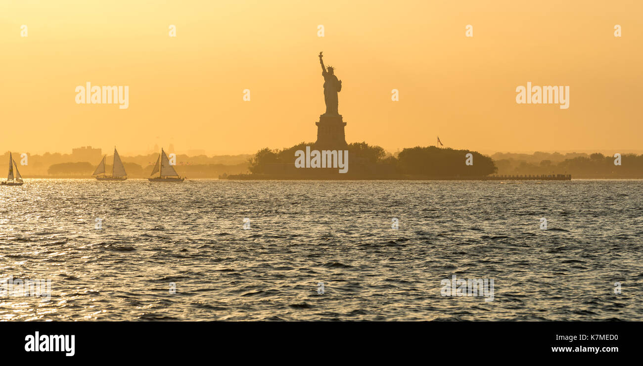 Freiheitsstatue und Liberty Island durch den New York Hafen mit Segelbooten im Sommer Sonnenuntergang Licht. New York City Stockfoto