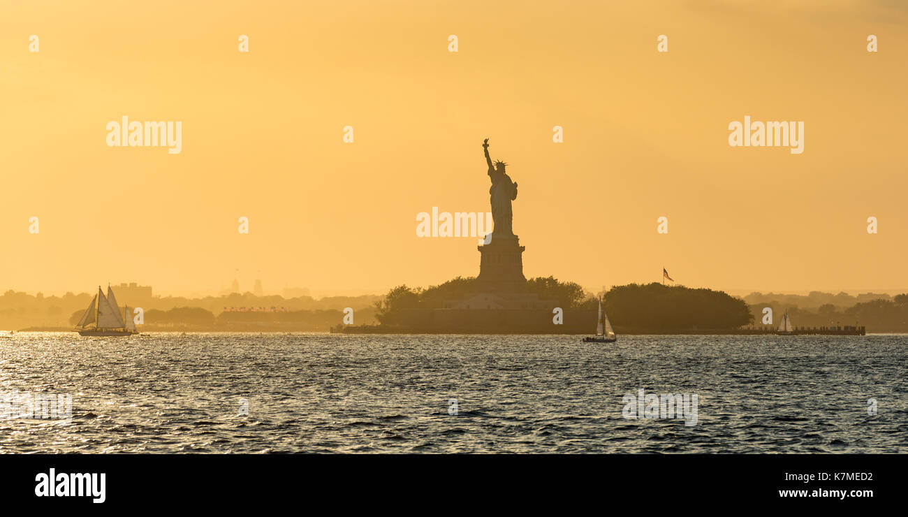 Freiheitsstatue und Liberty Island durch den New York Hafen mit Segelbooten im Sommer Sonnenuntergang Licht. New York City Stockfoto