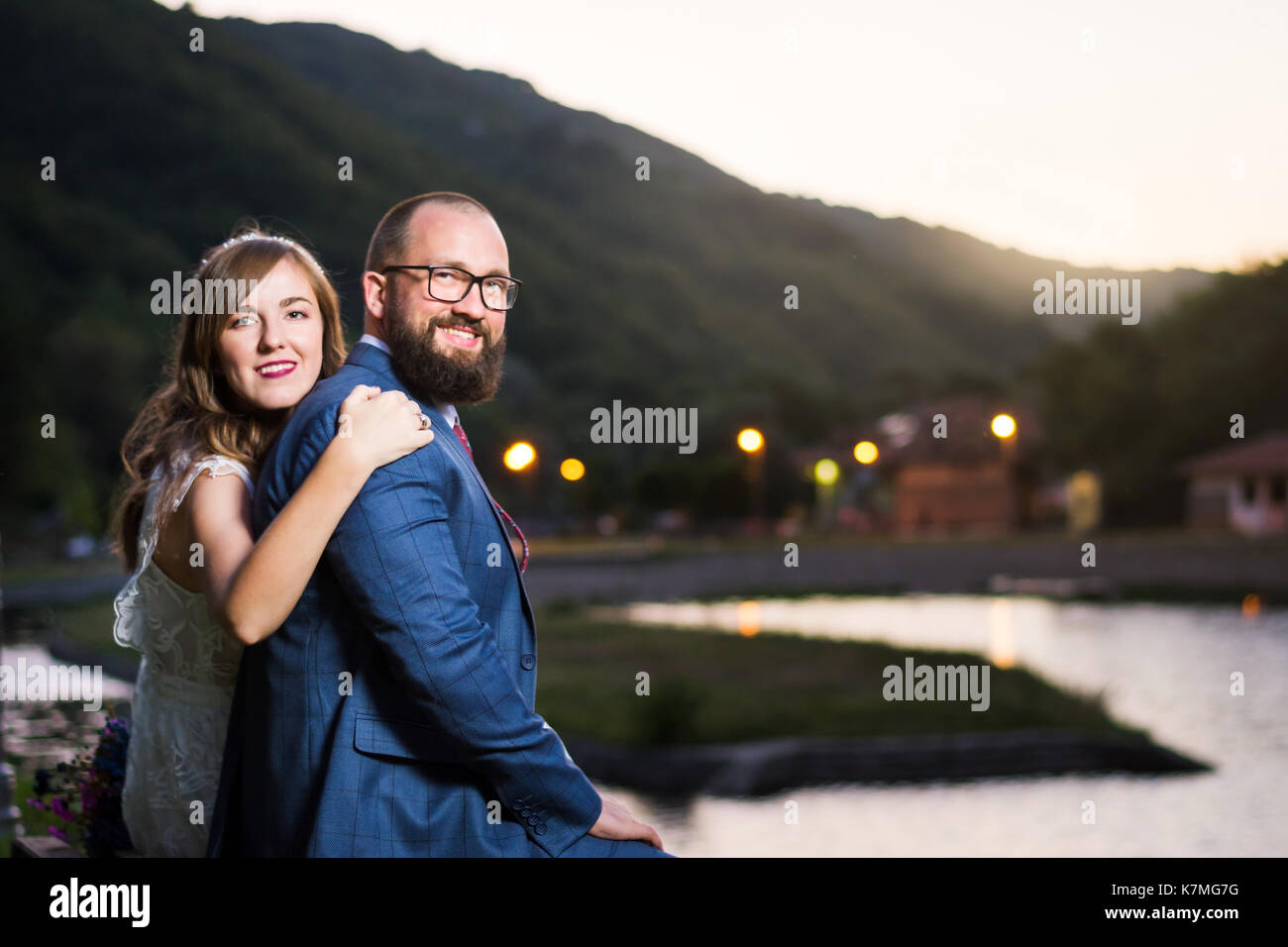Braut und Bräutigam sitzen am See am Abend Stockfoto