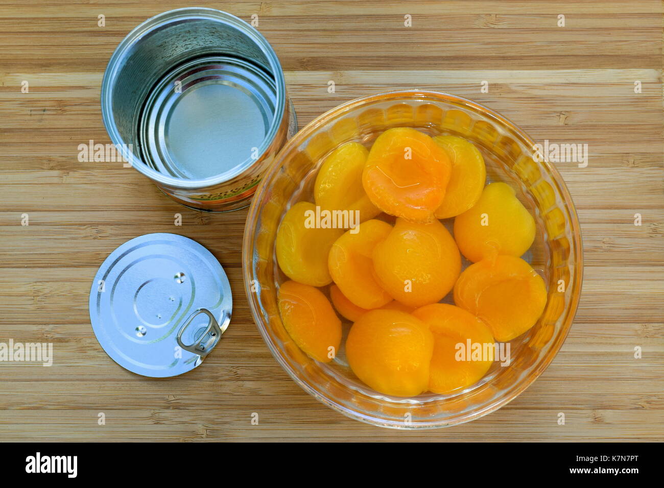 Aprikosen aus der Dose in Glasschale mit offenen Dose und Deckel auf Holzbrett Stockfoto