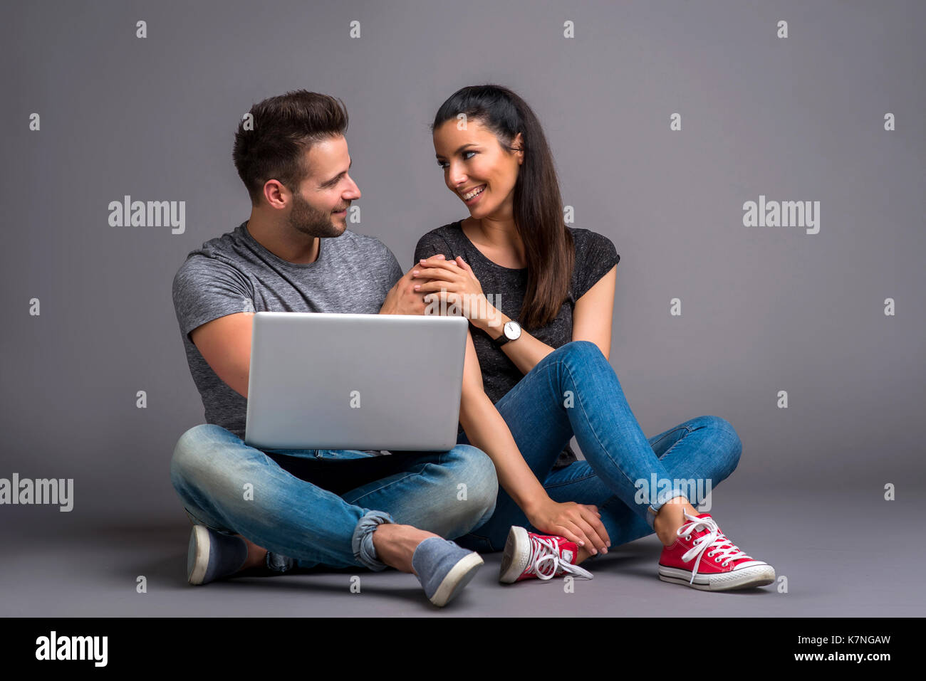 Ein schönes junges Paar auf dem Boden sitzend und mit Blick auf einen Laptop und lächelnd Stockfoto