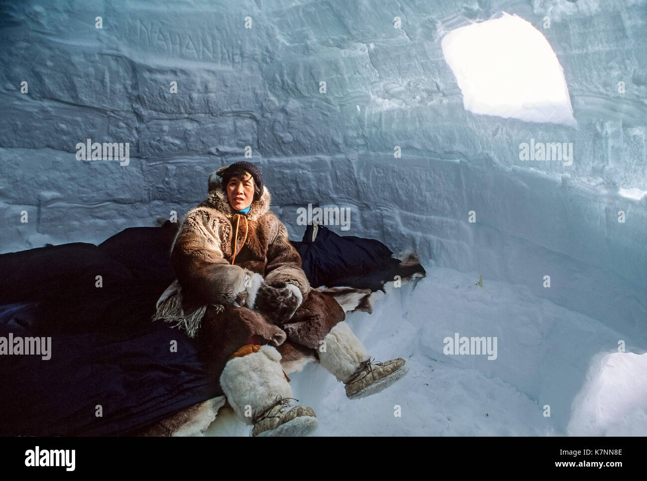 Besucher in traditionellen Caribou haut Kleidung sitzt auf Caribou Skins auf eine schlafende Sims im Iglu, wo sie Campingplatz für eine Woche. Außerhalb Baker Lake, Nunavut, Kanada. Hinweis Das Fenster. Es ist eine klare Block aus Eis. Stockfoto