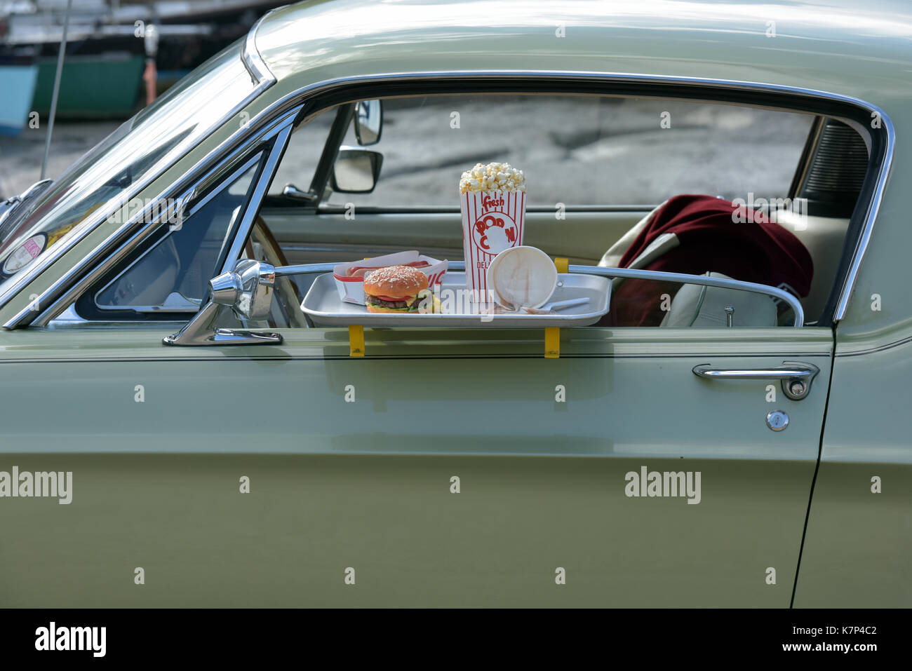 Ein Beef Burger und Pommes an die Tür eines klassischen Amerikanischen Auto auf eine Fahrt durch Gerichte zum Mitnehmen oder im Kino mit Popcorn. Fast Food Restaurants Stockfoto