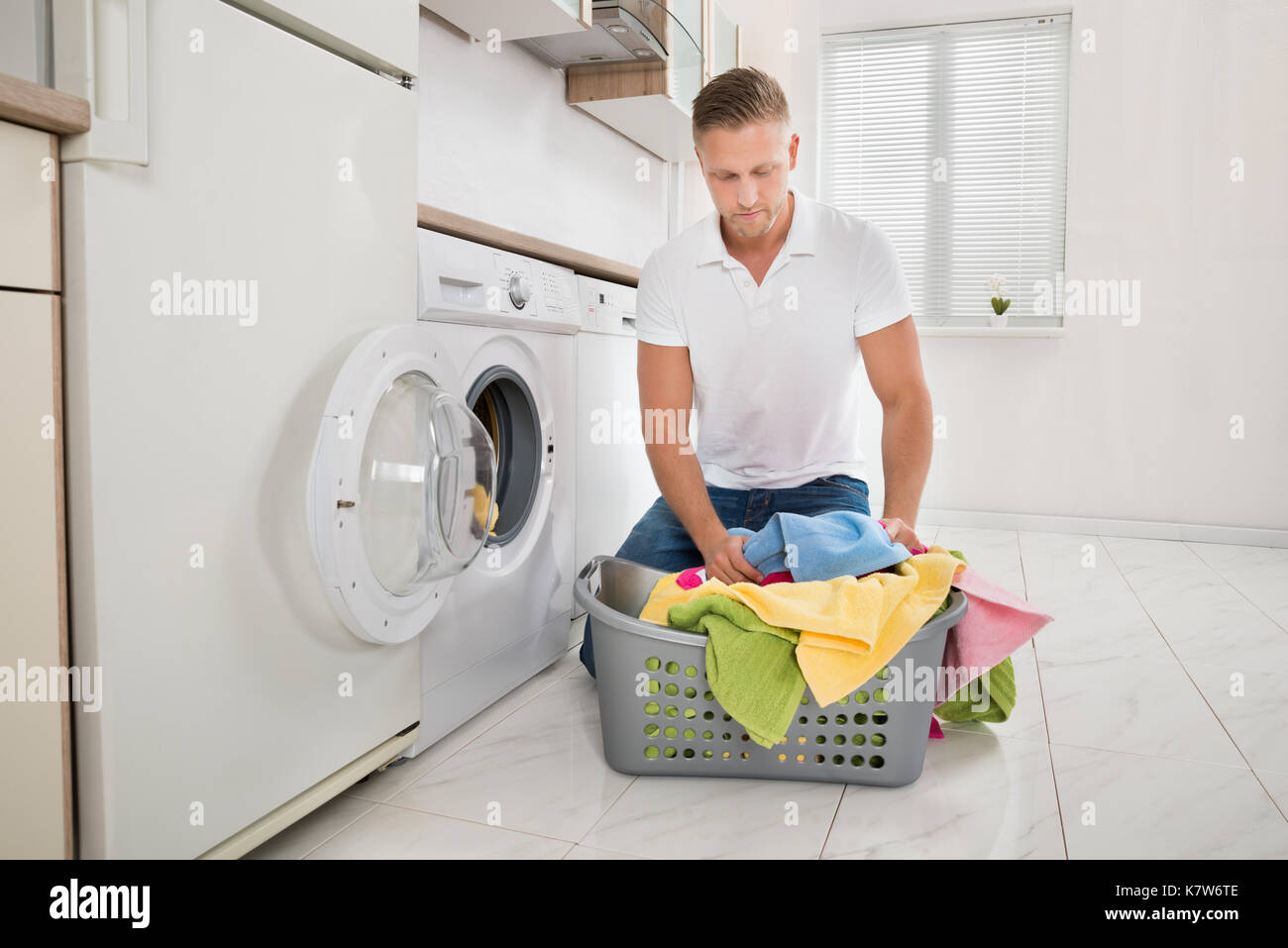 Junger Mann kniet auf dem Boden und setzen Bunte Handtücher in der Waschmaschine Stockfoto