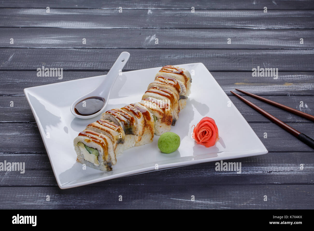 Kanada sushi Brötchen mit Lachs, Aal, Philadelphia Käse, Avocado und Gurke serviert auf weiße, flache Platte mit Stäbchen über blsck Hintergrund. Asiatische Stockfoto