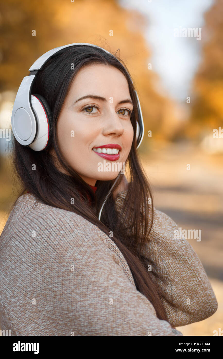 Junge glücklich lächelnde Frau mit Kopfhörer im Freien auf Herbst Tag. Mädchen Musik im Park. Herbst Porträt Stockfoto