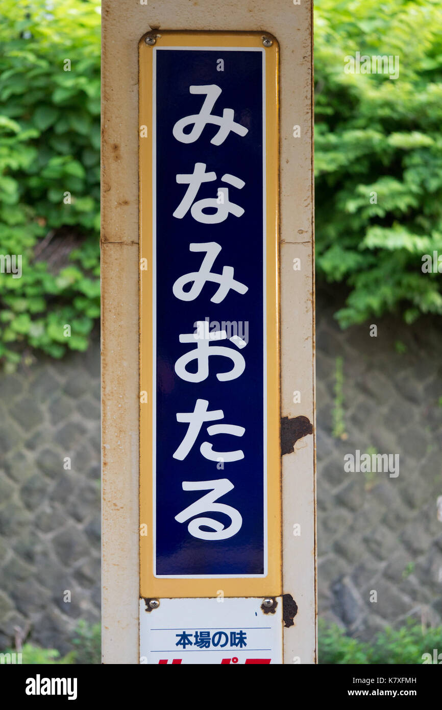 Close up Vertikale hiragana Blau Weiß und Gelb minami Otaru lokale JR Zug Plattform Schild mit grünem Efeu und traditionellen Stein Wand im Hintergrund. Stockfoto