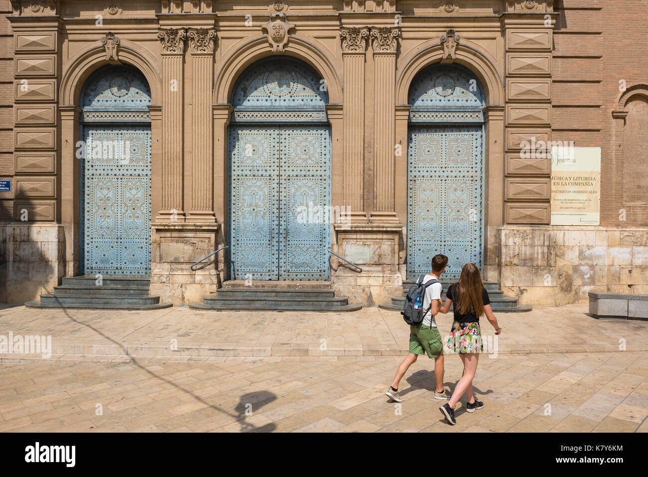 Reisen junge Leute, Rückansicht von zwei jungen Reisenden, die die Türen einer barocken Kirche betrachten, während sie durch die Altstadt von Valencia gehen. Stockfoto