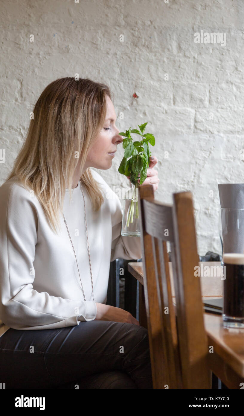 Junge Erwachsene blonde lange Haare erfreut, Frau riecht frischer Minze. Unposed candid vertikaler Stockfoto