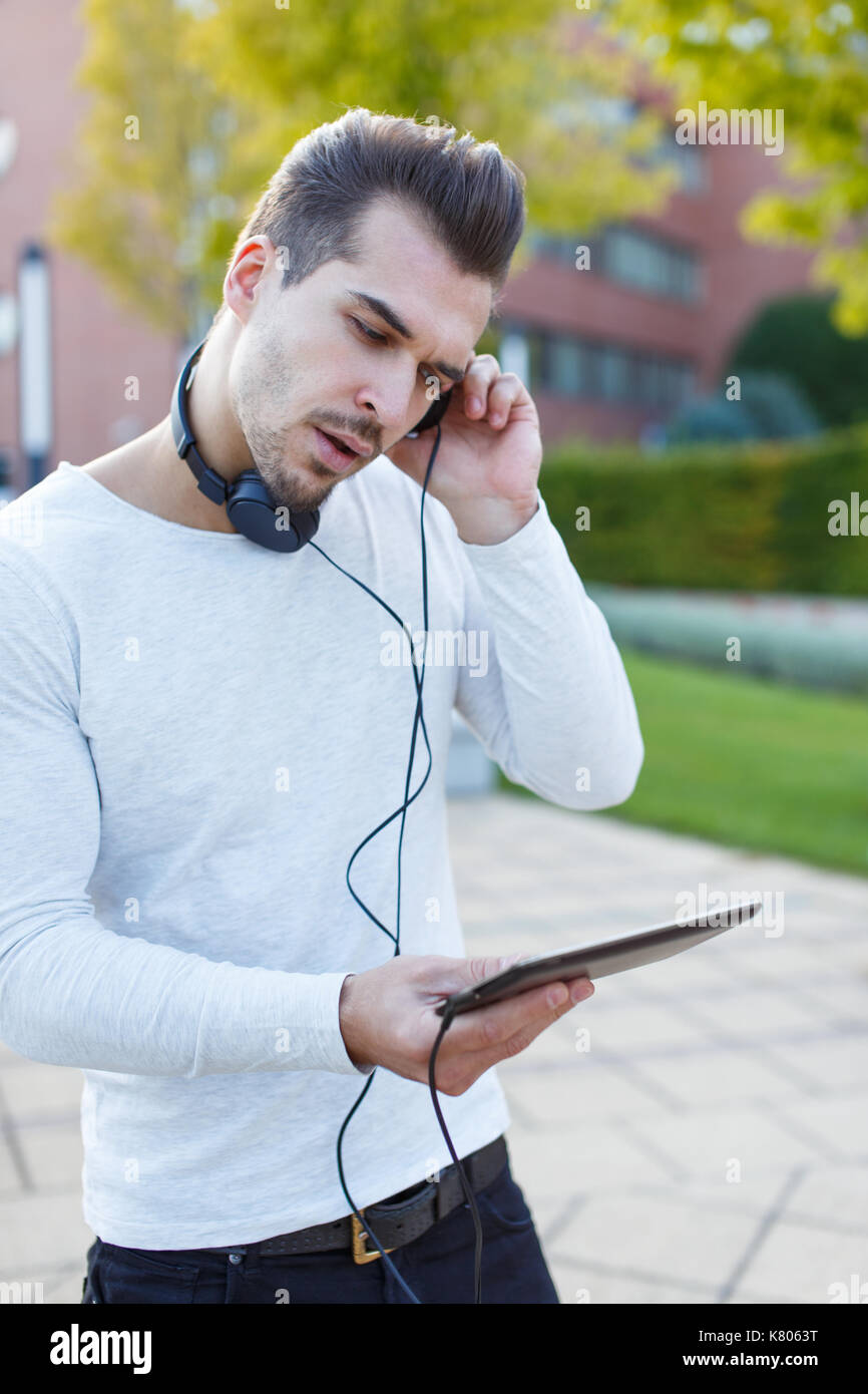Junger Mann hören Musik auf Tablet von hadphones Outdoor Stockfoto