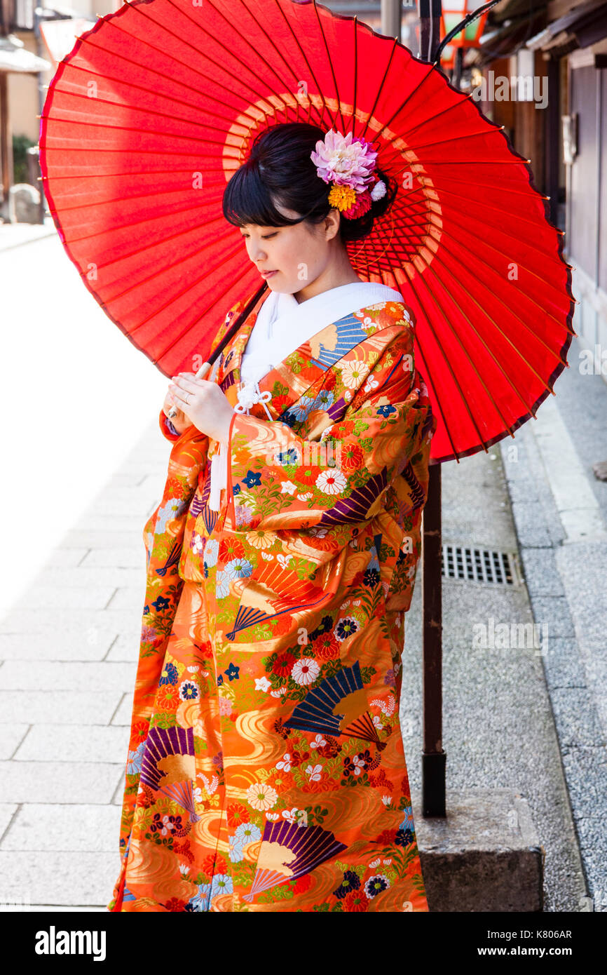 Japan, Kanazawa, Higashi Chaya. Seite - Japanische junge Frauen im Kimono ständigen Blick und halten grosse rote parsole. Blumen im Haar. Stockfoto