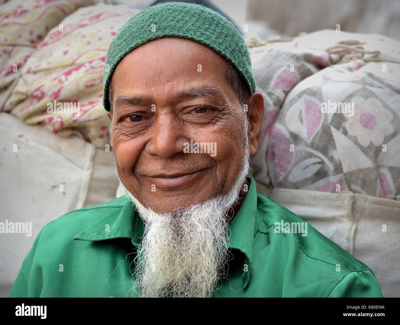 Älterer indischer Moslem-Mann mit weißem muslimischen Kinnbart trägt ein grünes Hemd und eine gestrickte grüne muslimische Gebetskappe (taqiyah) und lächelt für die Kamera. Stockfoto