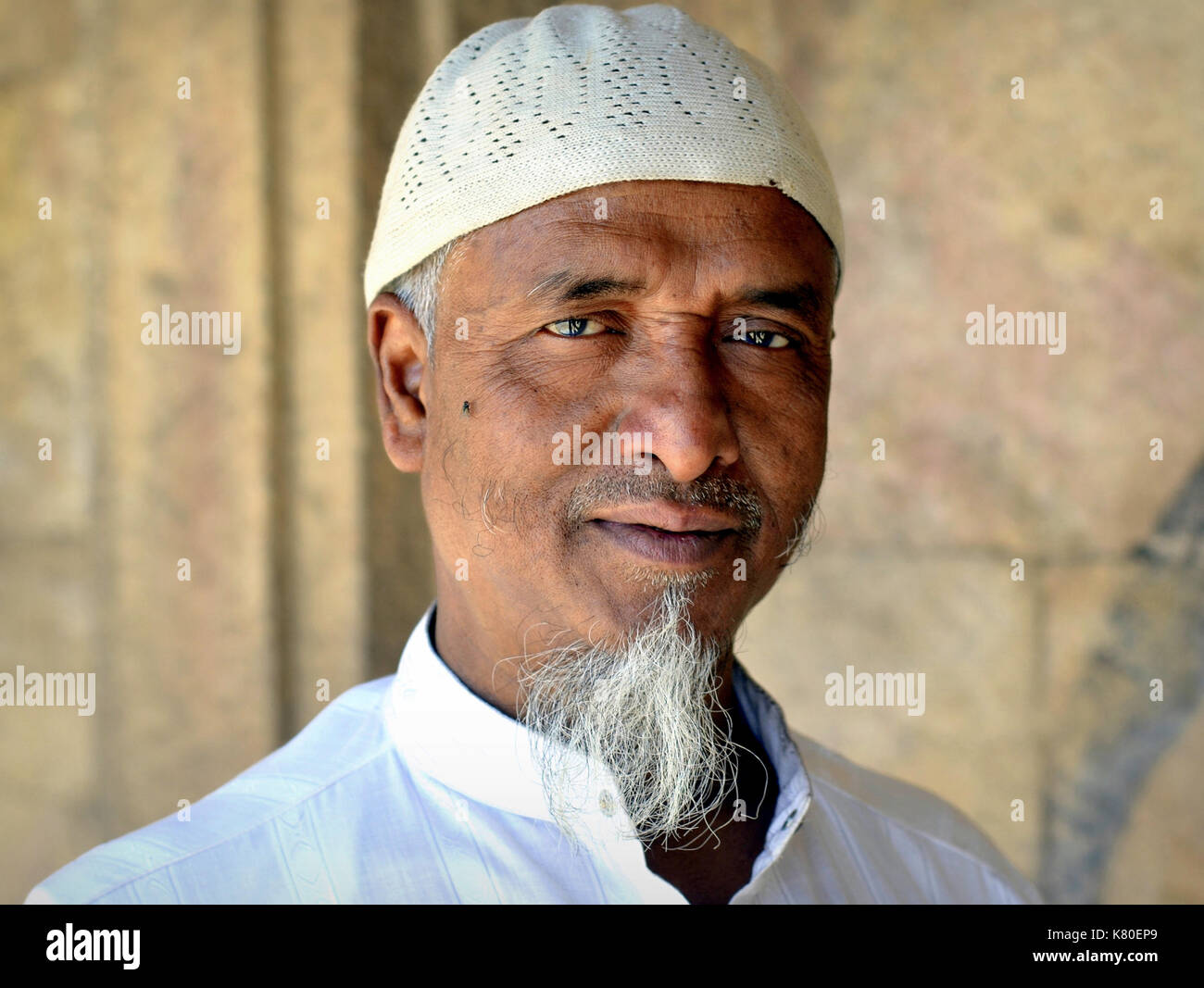 Indianischer Moslem-Mann mittleren Alters mit muslimischem Ziegenleder, der eine weiße islamische Betkappe (Taqiyah) trägt und für die Kamera posiert. Stockfoto