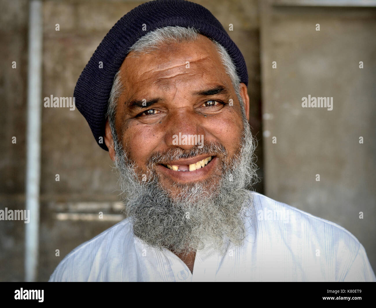 Älterer indischer Moslem-Mann mit islamischem Bart, Zahnlücke und muslimischem Gebetstich (Zebibah) auf der Stirn lächelt für die Kamera. Stockfoto