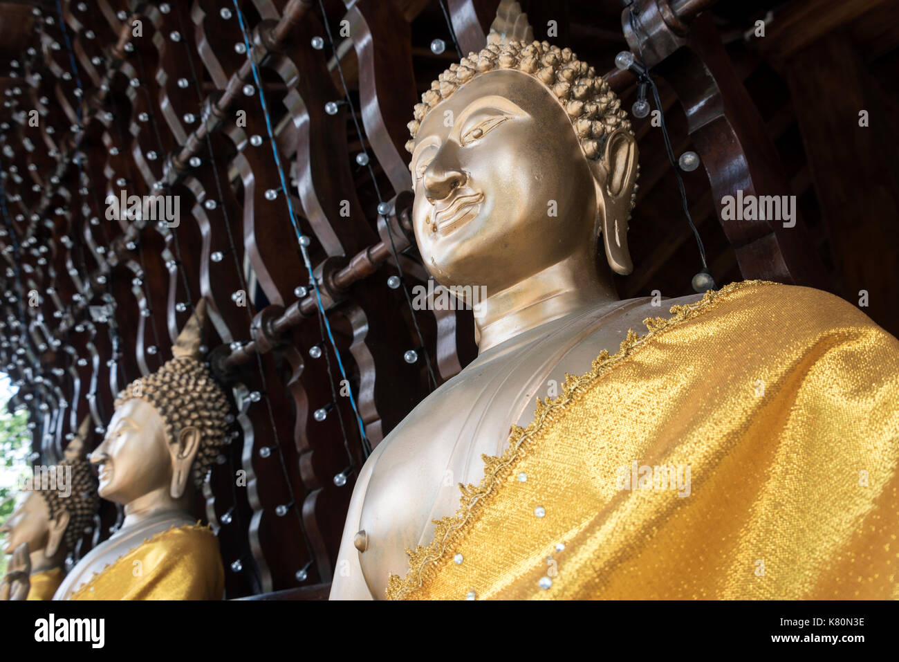 Eine Reihe buddhistischer Statuen, die in gelbes Tuch gehüllt sind, an einer Wand des Seema Malakaya Tempels, der sich auf einer kleinen Insel am Beira-See entlang des Sir James Pier befindet Stockfoto