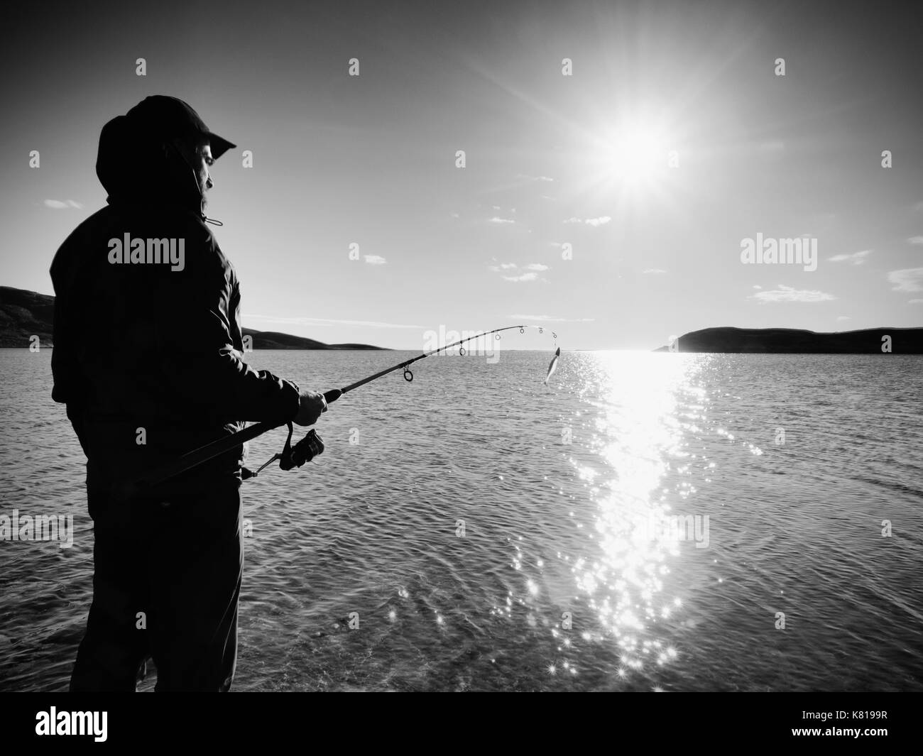Fischer prüfen Angeln und Köder auf der Stange, selbst vorbereiten und weit in das ruhige Wasser locken werfen. Fischer Silhouette bei Sonnenuntergang Stockfoto