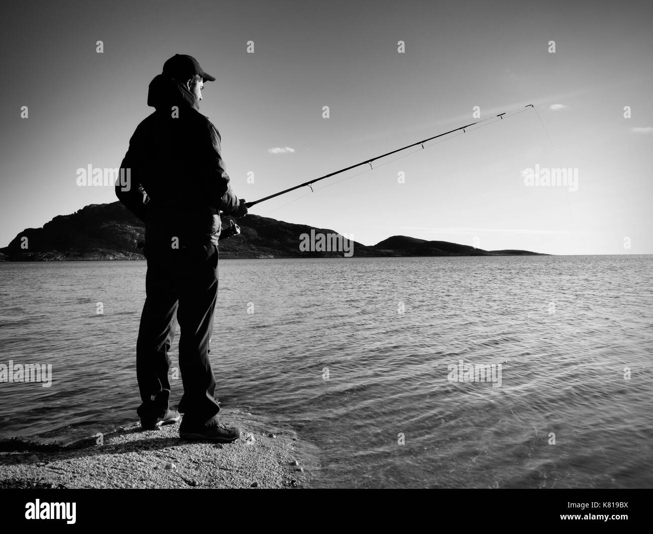 Fischer prüfen Angeln und Köder auf der Stange, selbst vorbereiten und weit in das ruhige Wasser locken werfen. Der erwachsene Mann in warme Kleidung ist fis Stockfoto