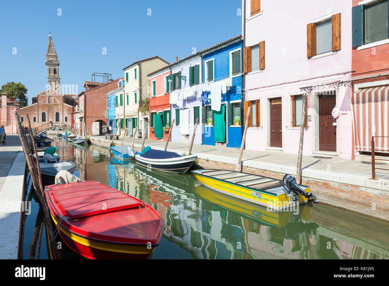 Chiesa oder die Kirche San Martino und die schiefen Kirchturm, Burano, Venedig, Venetien, Italien gesehen in den Kanal mit bunten angelegten Boote wider Stockfoto