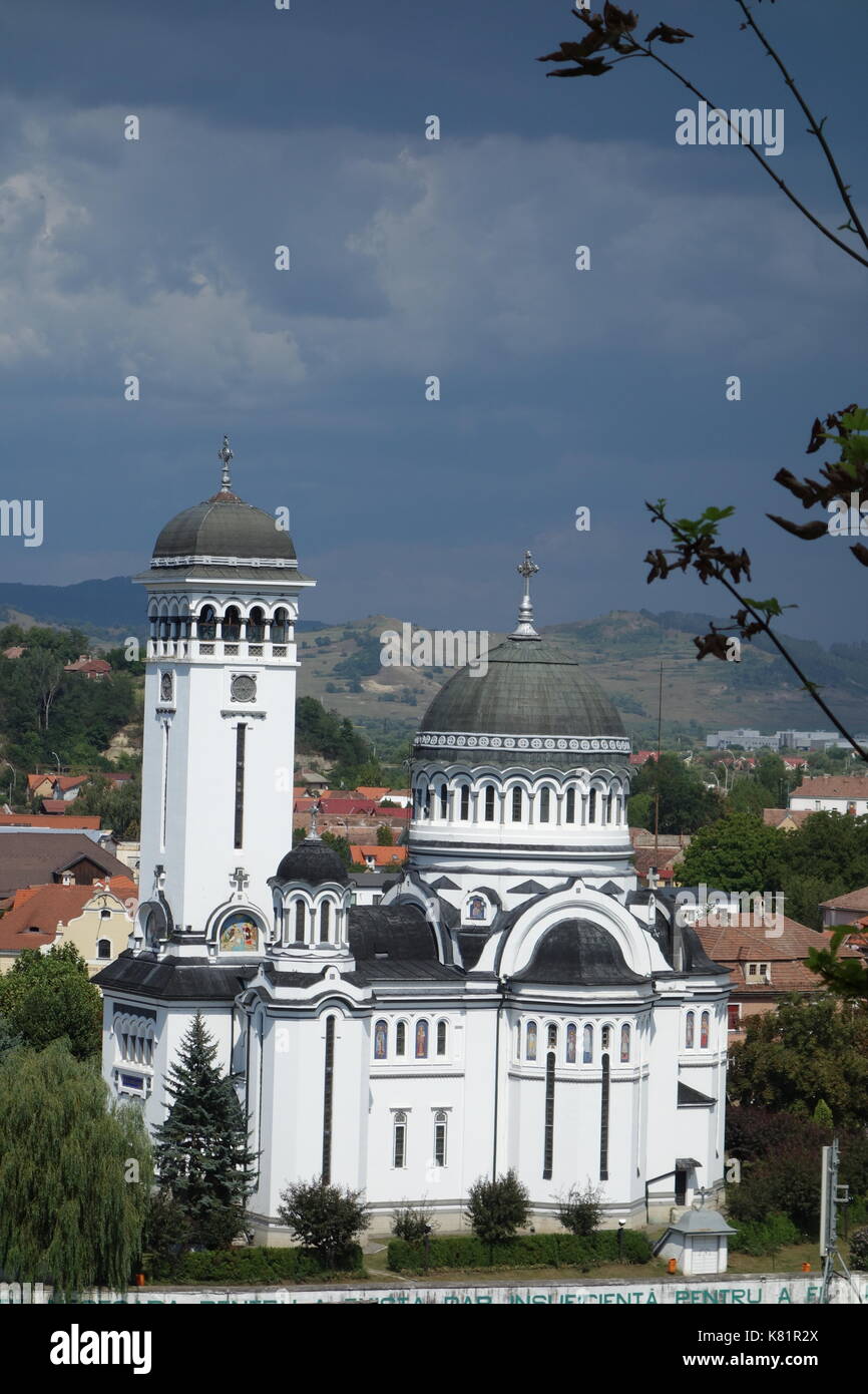 Dreifaltigkeitskirche mit rumänischer Flagge und wolkenverirlter Himmel. Sighisoara, Siebenbürgen, Rumänien Stockfoto