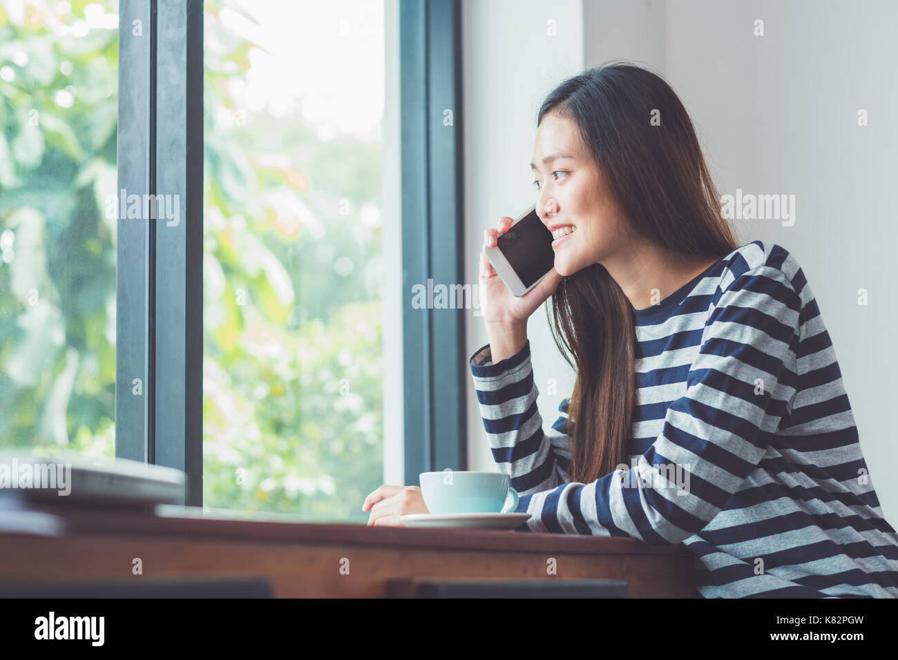 Asiatische Frau Gespräch am Handy und Sitzen im Cafe Restaurant in der Nähe der Fenster durch Garten, Digital Lifestyle, Arbeiten außerhalb der Begriff Stockfoto