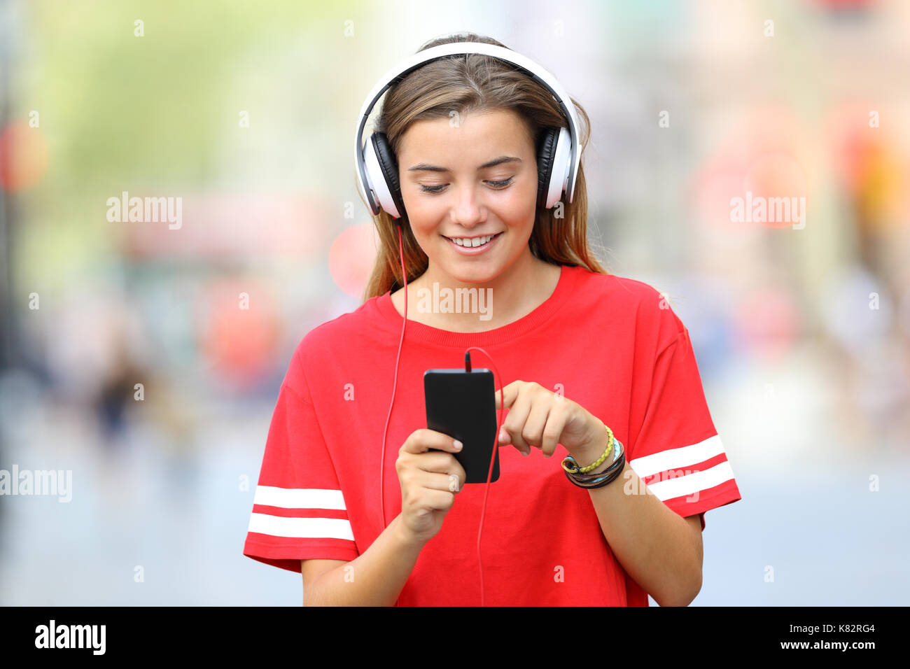 Vorderansicht eines einzigen jugendlich Mädchen gehen und Musik hören auf der Straße Stockfoto