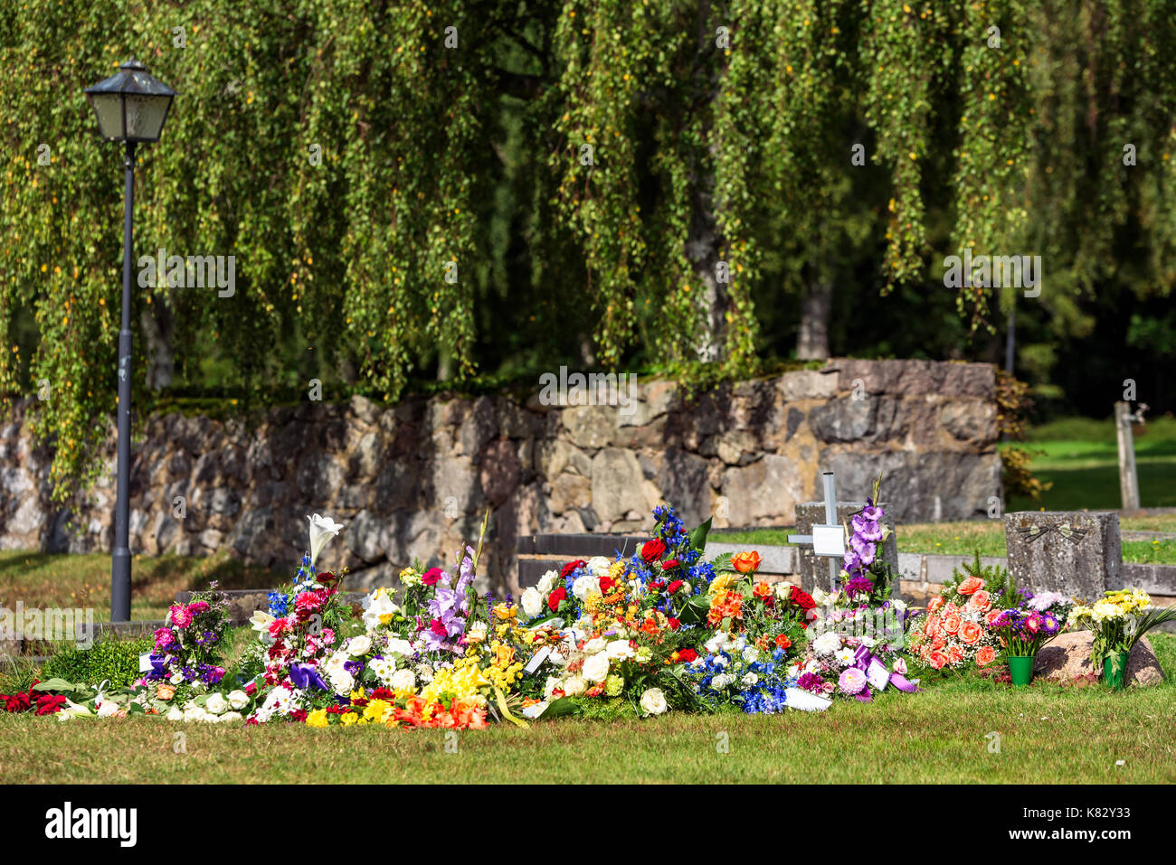 Vielen Blumen und kleine Kreuz nach einer Trauerfeier auf einem Friedhof. Name und Text entfernt von allen Notizen und Tags. Stockfoto