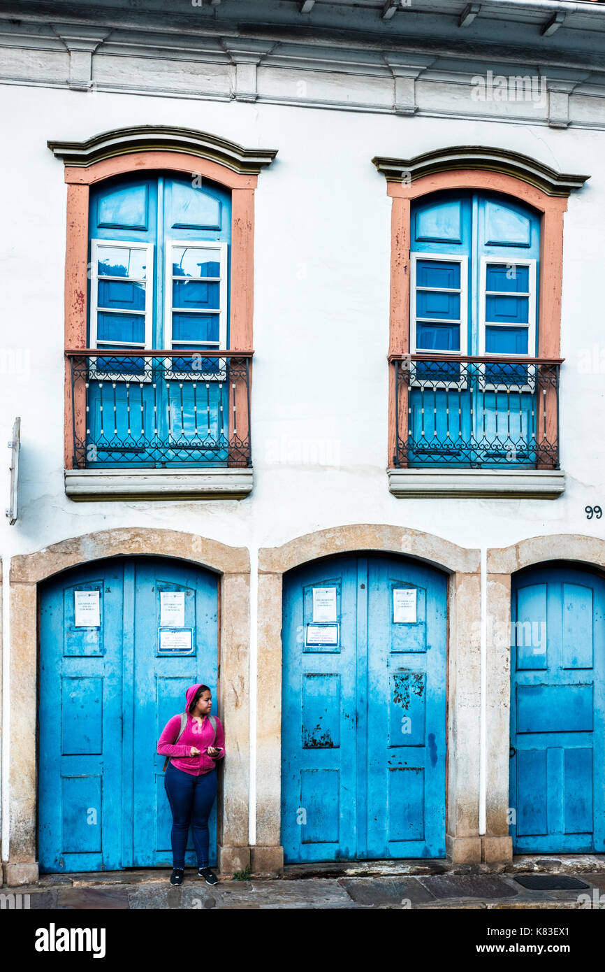 Eine junge Frau, die für den Transport vor einem Haus im Kolonialstil in Ouro Preto, Minas Gerais, Brasilien. Stockfoto