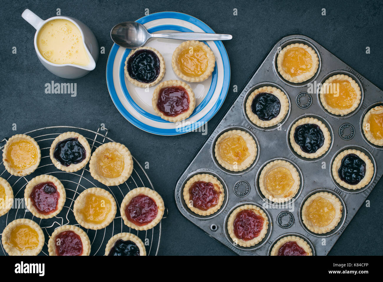 Zubereitet hausgemachte Marmeladentörtchen auf einem Teller mit Vanillesauce neben einem backblech und ein Vintage kreisförmigen Gitter Stockfoto