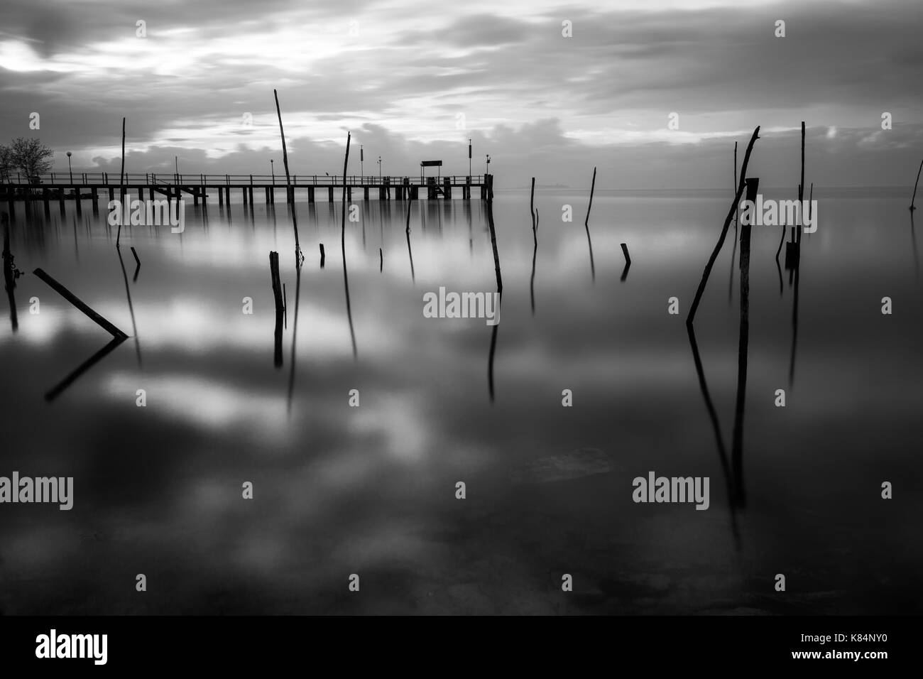 Surreal lange Belichtung Blick auf den See, mit Holzstangen auf perfekt noch Wasser und ein Pier im Hintergrund Stockfoto