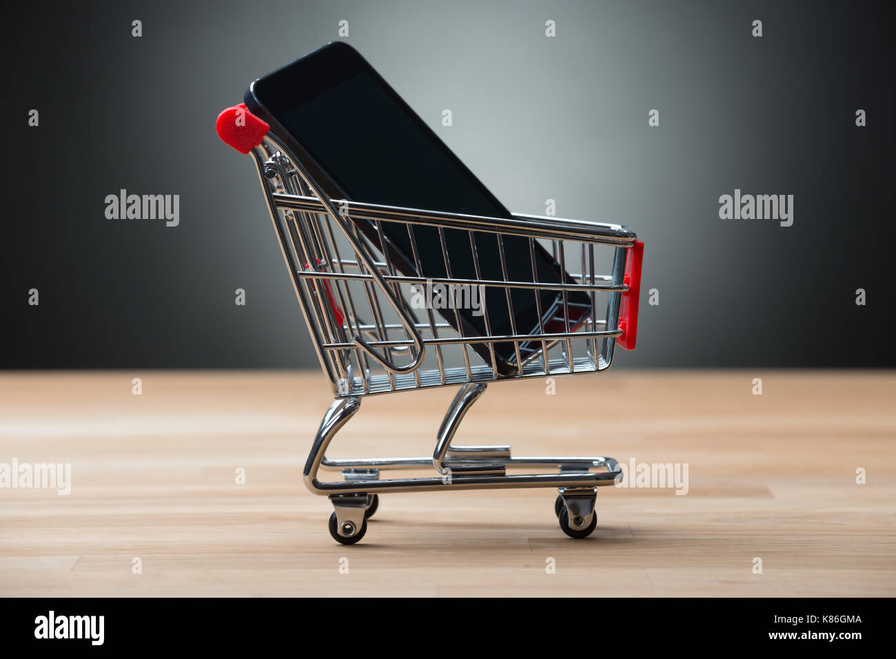 Nahaufnahme des Smartphones im Warenkorb auf hölzernen Tisch gegen grauer Hintergrund Stockfoto