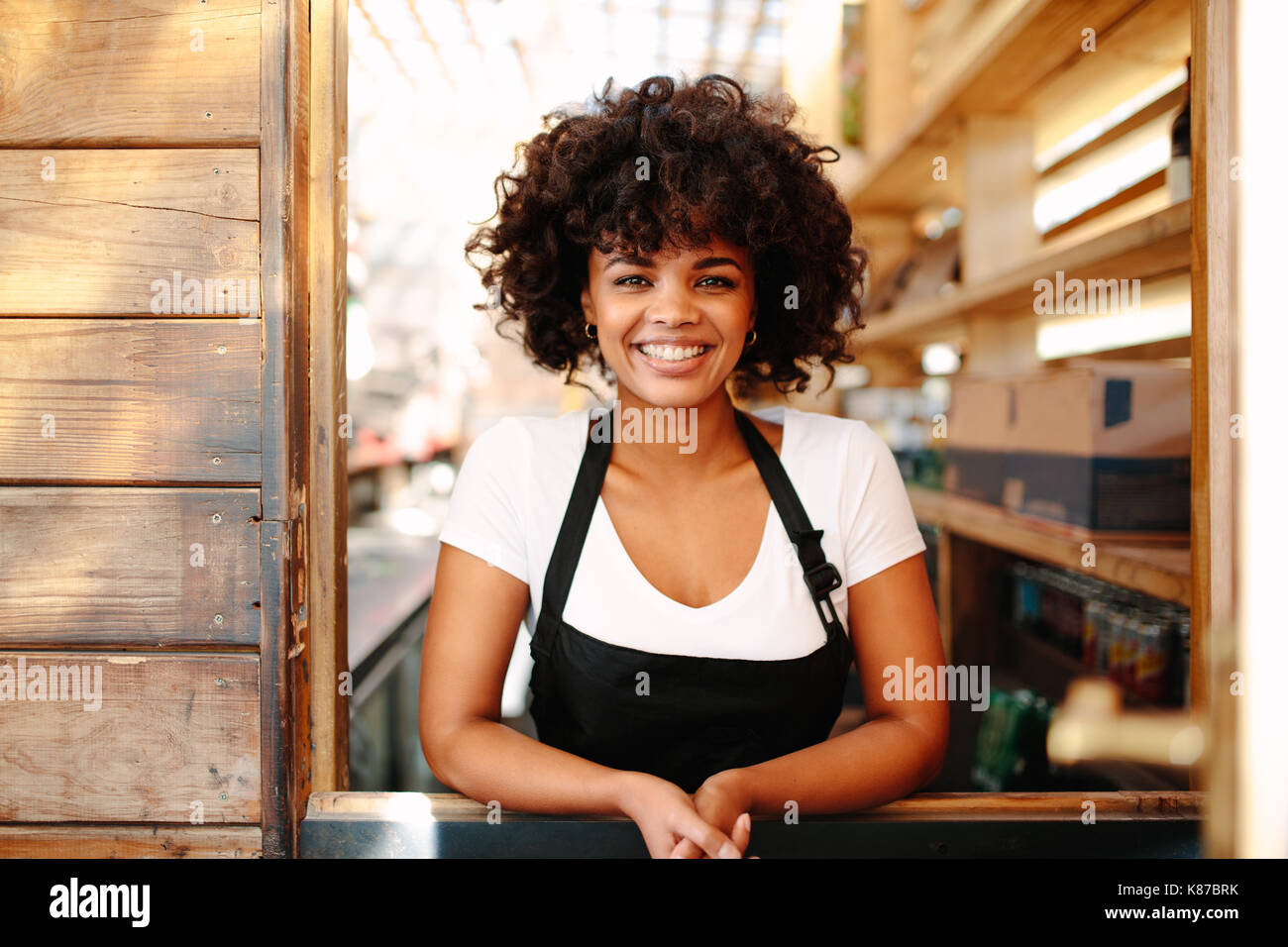 Frau barista in Ihr Coffee Shop. Curly behaarte Frau Barkeeper in fröhlicher Stimmung hinter der Theke. Stockfoto