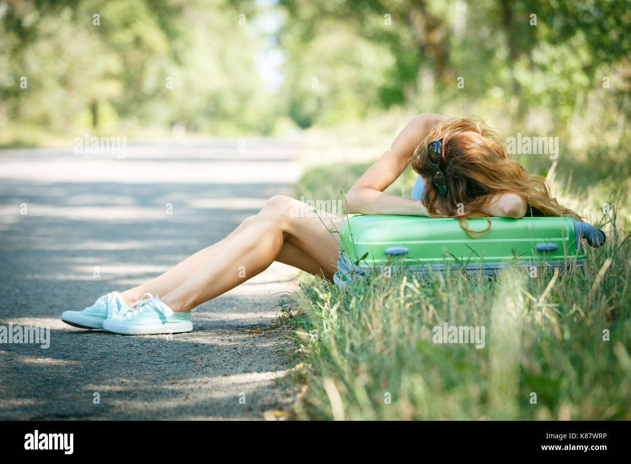 Per Anhalter Mädchen im Sommerkleid schlafen Müde lehnte sich auf einen Fall. Stockfoto