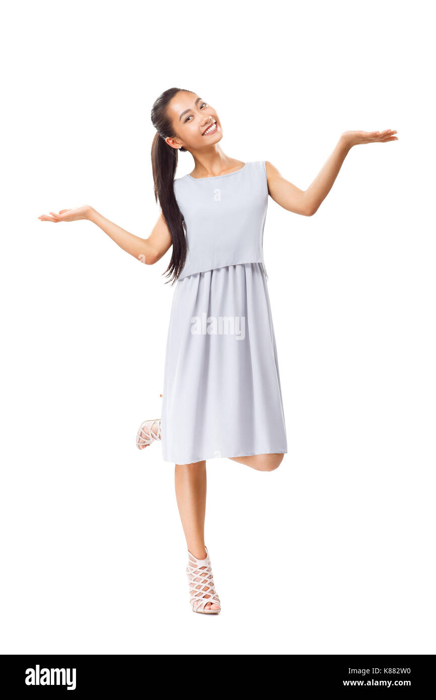 Lächelnde junge asiatische Frau in graues Kleid und High Heels Stehen auf einem Bein, hand Balance und Kamera. In voller Länge Porträt der weiblichen Stockfoto