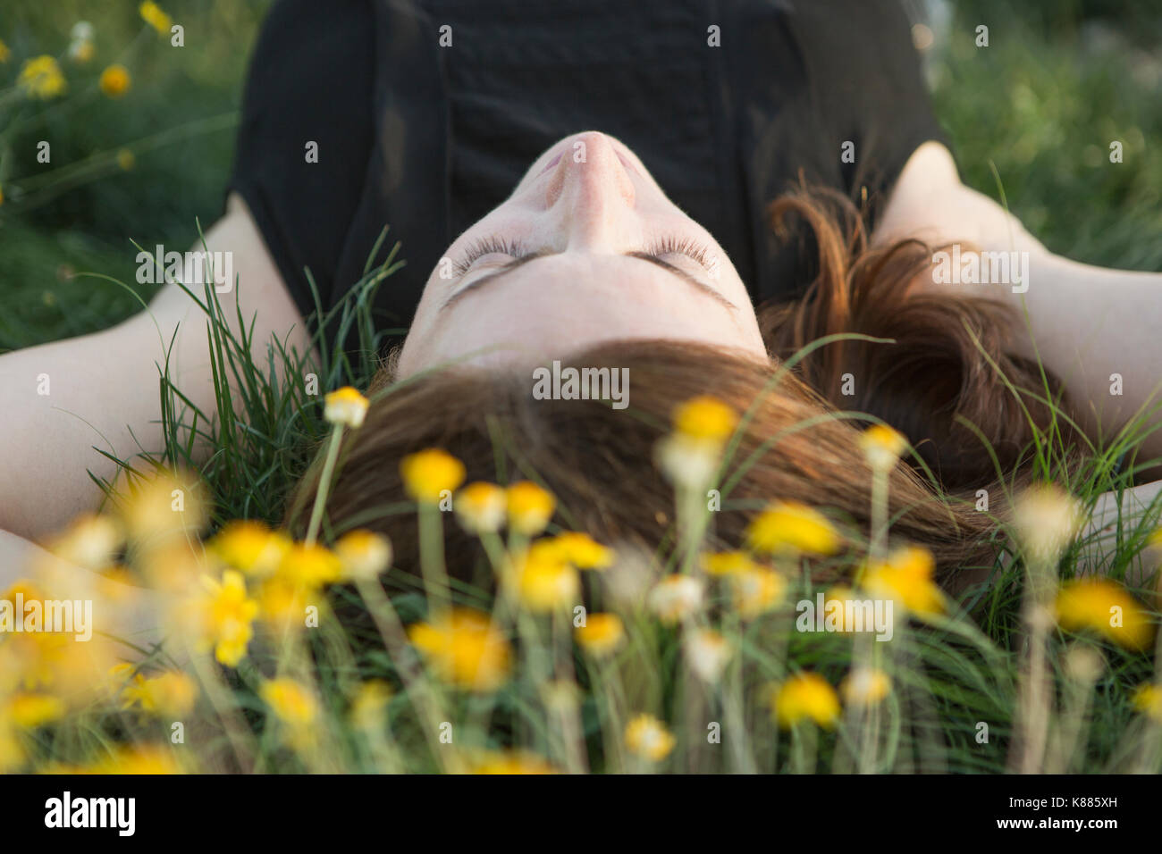 Eine Frau in einem schwarzen Weste Top und Jeans, die auf dem Gras mit ihren Händen hinter dem Kopf. Stockfoto