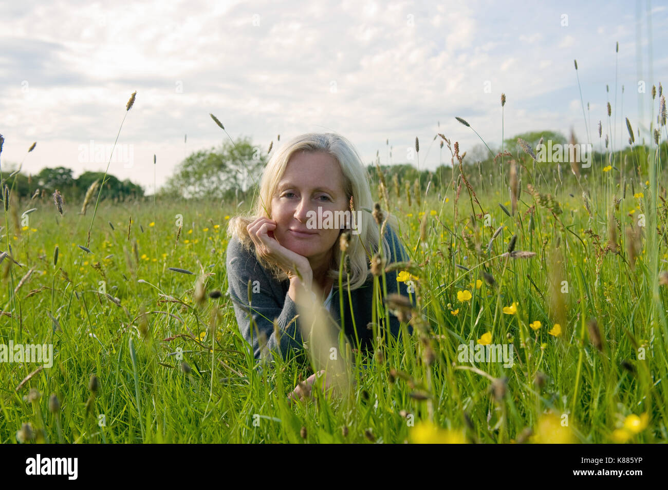 Portrait von blonde Frau liegt auf dem vorderen auf einer Wiese, Hand am Kinn, in die Kamera lächeln. Stockfoto