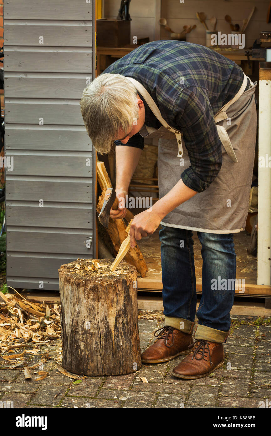 Handwerker Holzschnitzer Bücken und Halten einer Hand ax, schneiden ein kleines Stück Holz auf eine Aufspaltung blockieren. Stockfoto