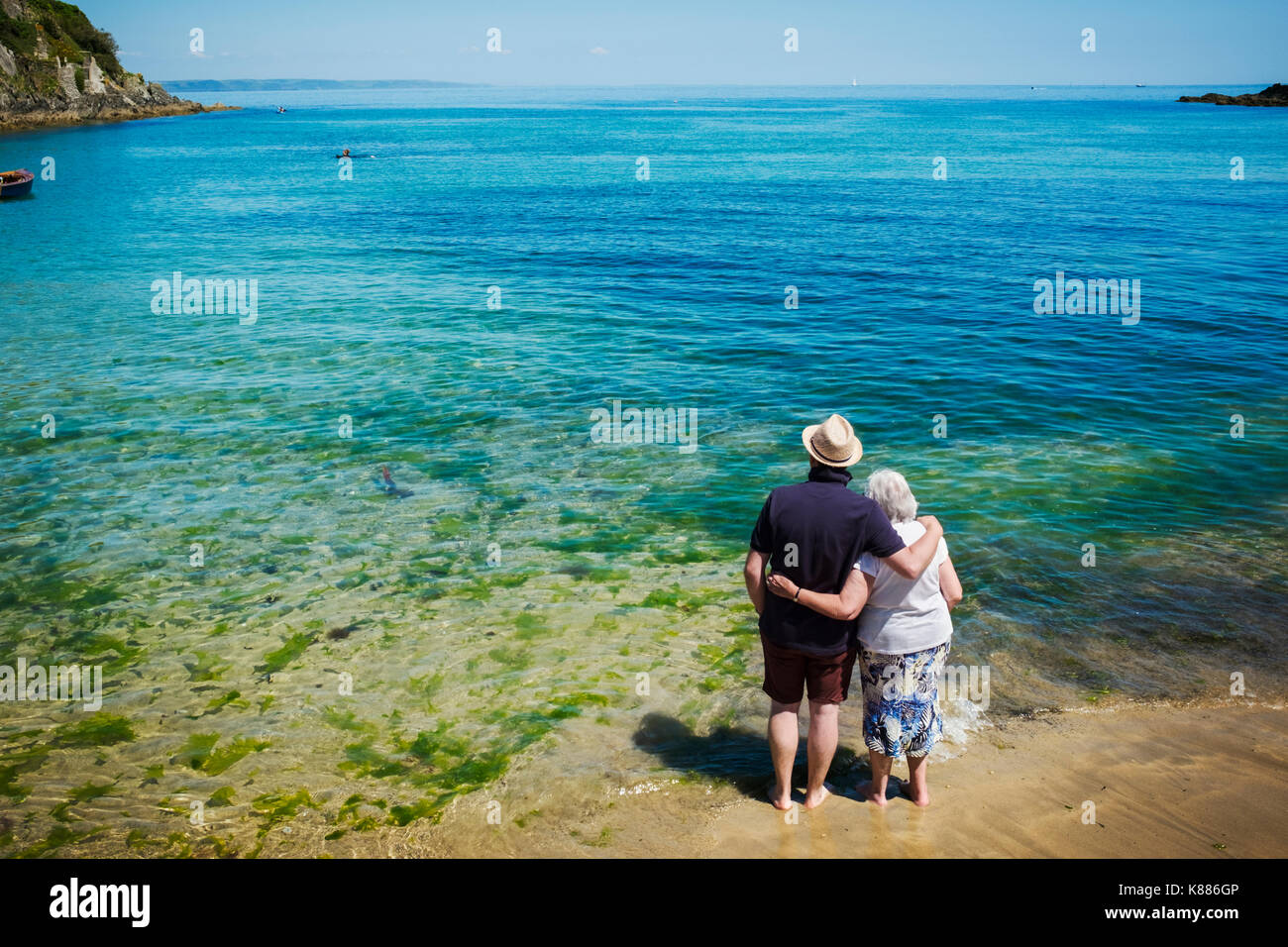 Ansicht der Rückseite des älteren Paares stehend mit Arme um einander über den strahlend blauen und türkisfarbenen Wasser suchen, das Meer. Stockfoto