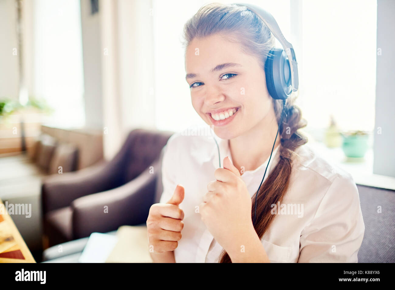 Positive Mädchen in Kopfhörer auf Kamera mit toothy Lächeln und genießen Sie Songs aus der Wiedergabeliste Stockfoto