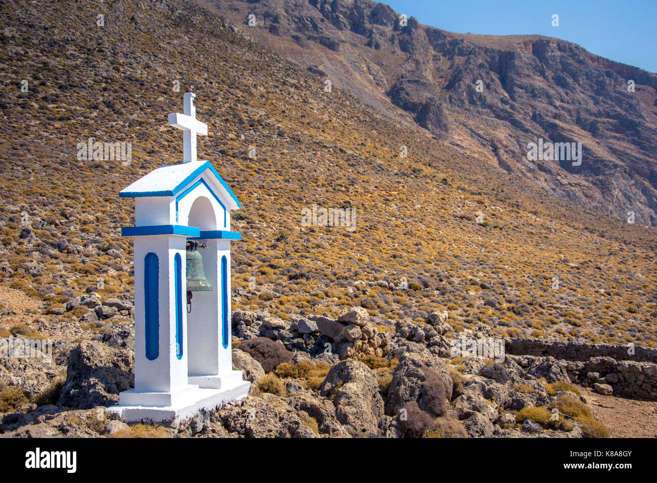 Weiße Glockenturm einer Kirche neben dem blauen Meer, an einem sonnigen Tag, Loutro, Chania, Kreta, Griechenland. Stockfoto