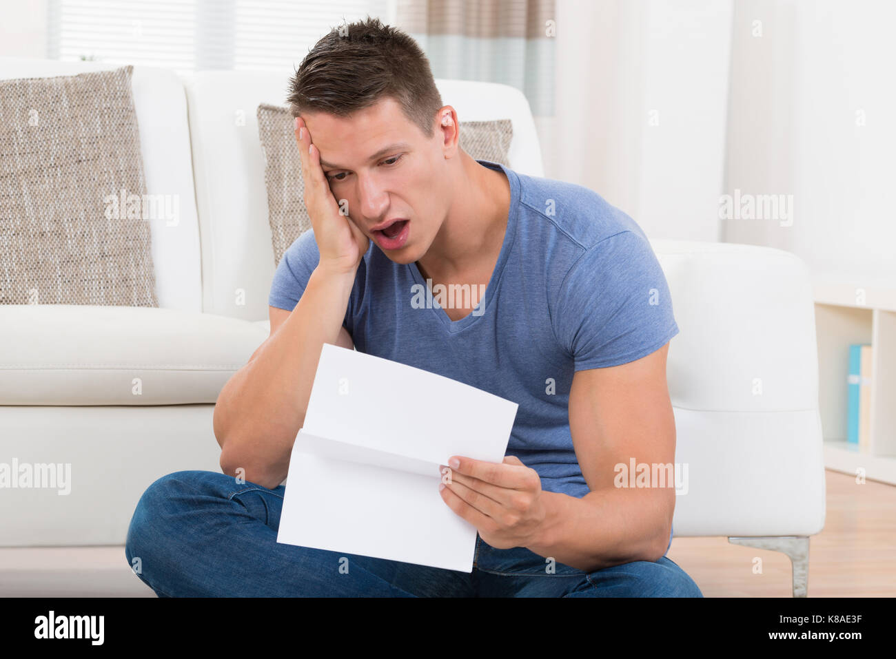 Schockiert, junger Mann auf der Suche nach Papier im Wohnzimmer Stockfoto