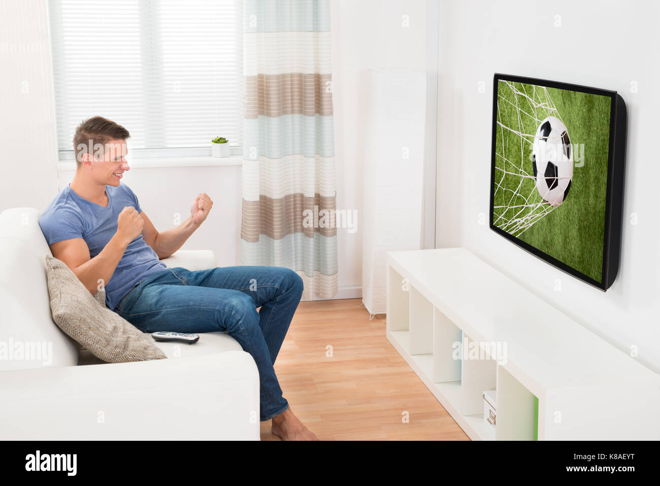 Glücklich Mann sitzt auf einem Sofa anschauen Sport im Fernsehen Stockfoto