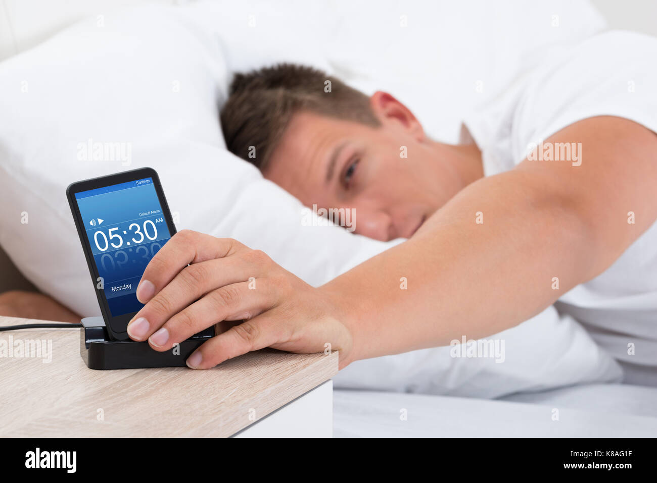 Junger Mann auf dem Bett dösen Wecker auf Handy Bildschirm Stockfoto