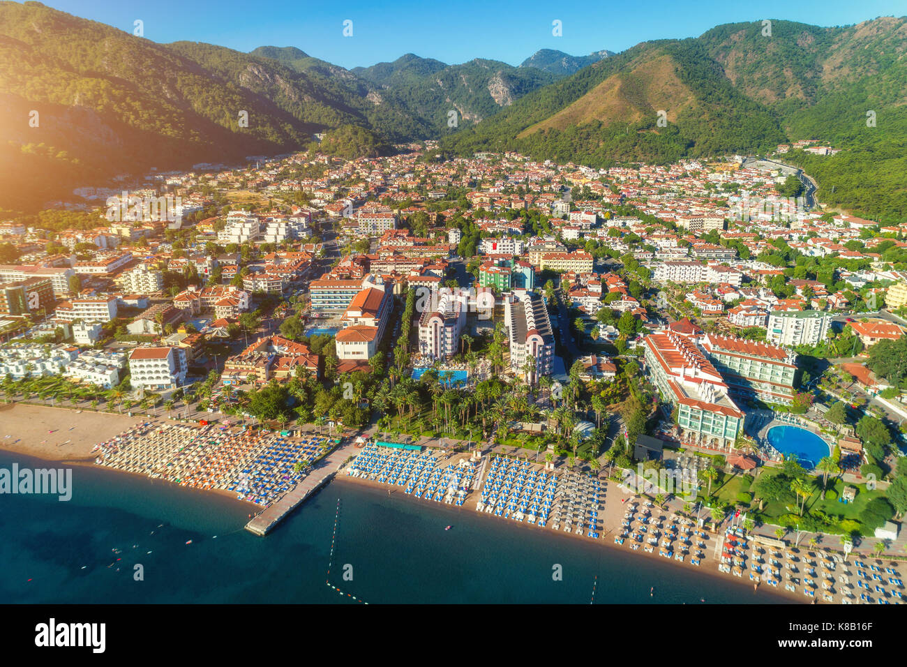 Luftaufnahme der schönen Stadt, Sandstrand mit Liegen - Lounges, Berge, grüne Bäume, Hotels, Gebäude, Pool, bei Sonnenuntergang in Icmeler, Türkei. Sommer Stockfoto