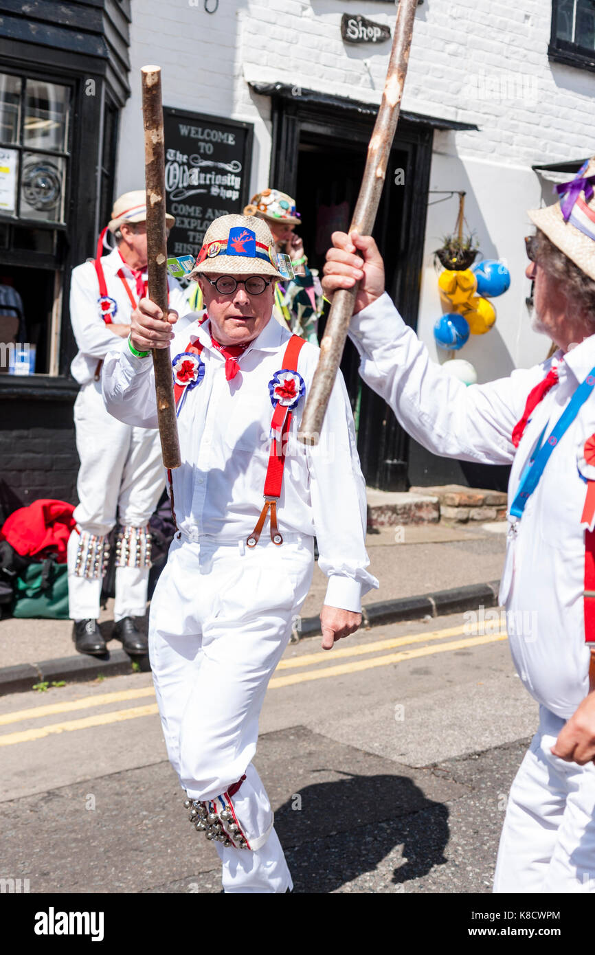 Traditionelle englische Hartley Morris Dancers in weißem Hemd und Hose mit roten Klammern und Strohhüte, Tanzen auf der Straße, und halten Holzpfähle Stockfoto