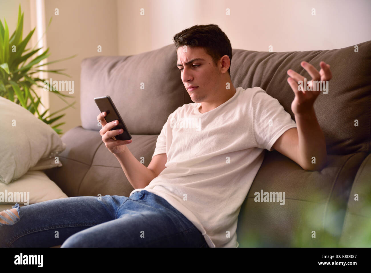 Teenager in der Auseinandersetzung mit Nachrichten auf dem Smartphone sitzt auf einem Sofa zu Hause empfangen Stockfoto
